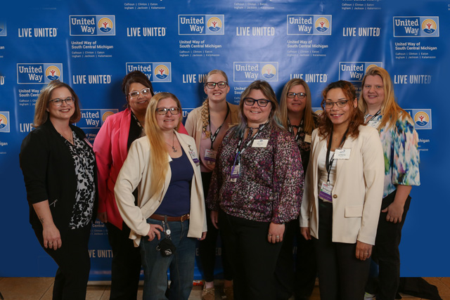 Eight people pose in front of United Way backdrop
