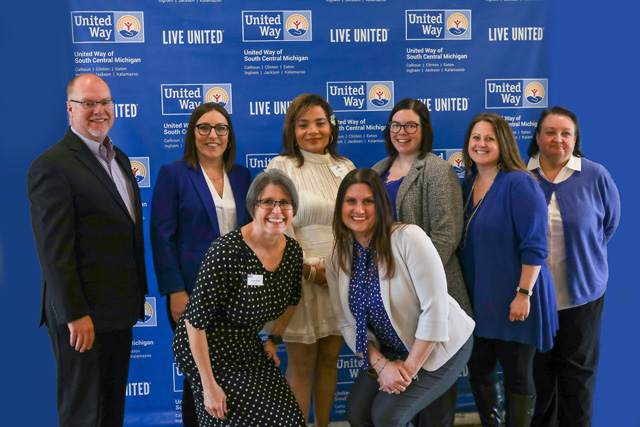 Eight people pose in front of United Way backdrop