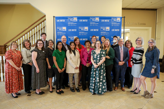 19 United Way staff members pose in front of United Way backdrop.