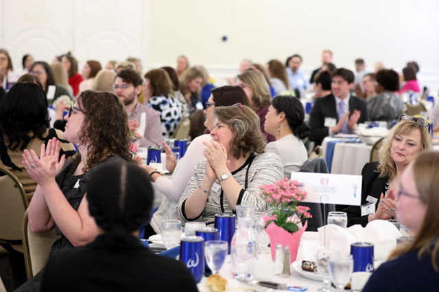 Men and women sit at tables clapping.