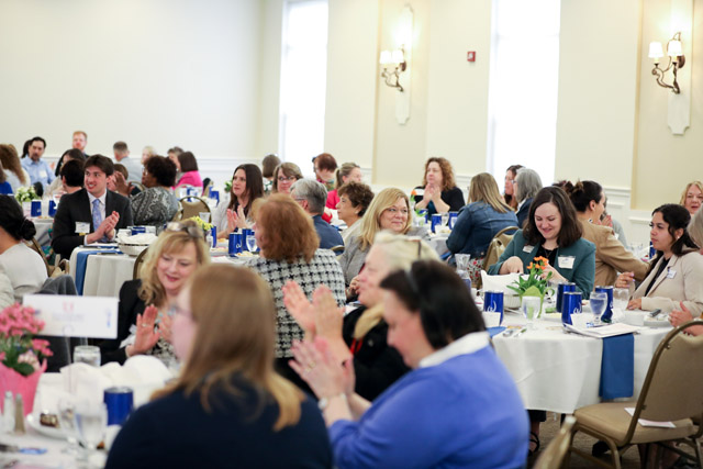 Men and women sit at tables clapping.