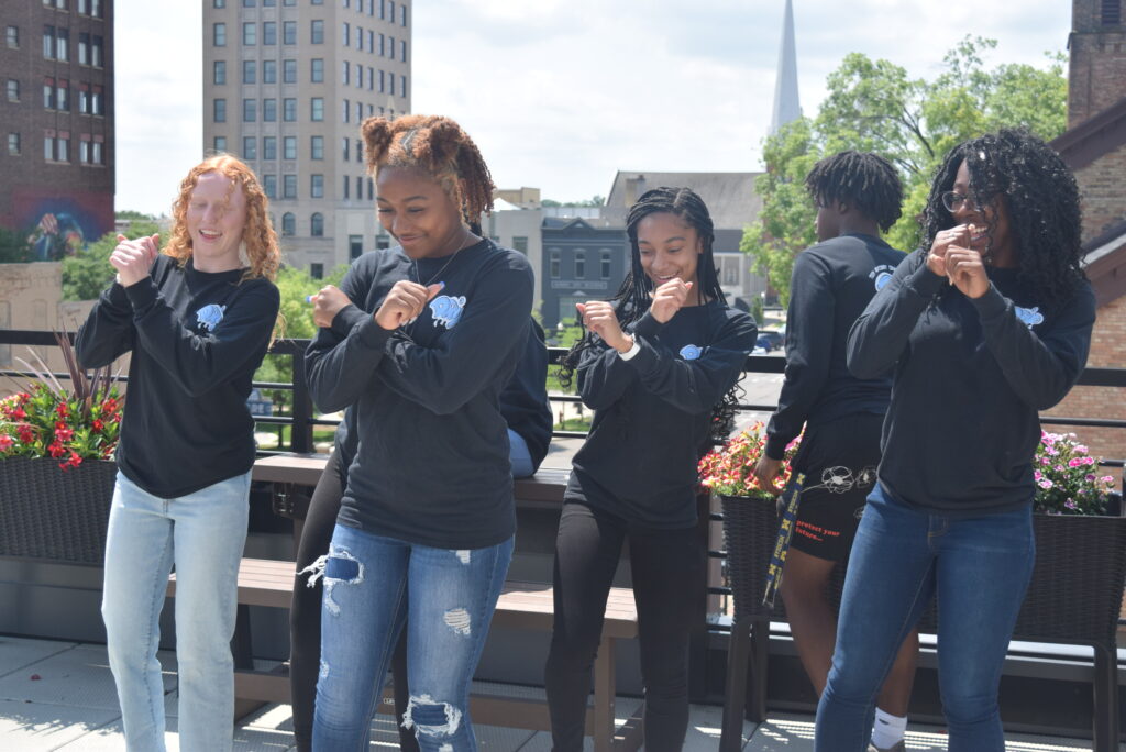Teens in matching shirts dance atop a Jackson rooftop.