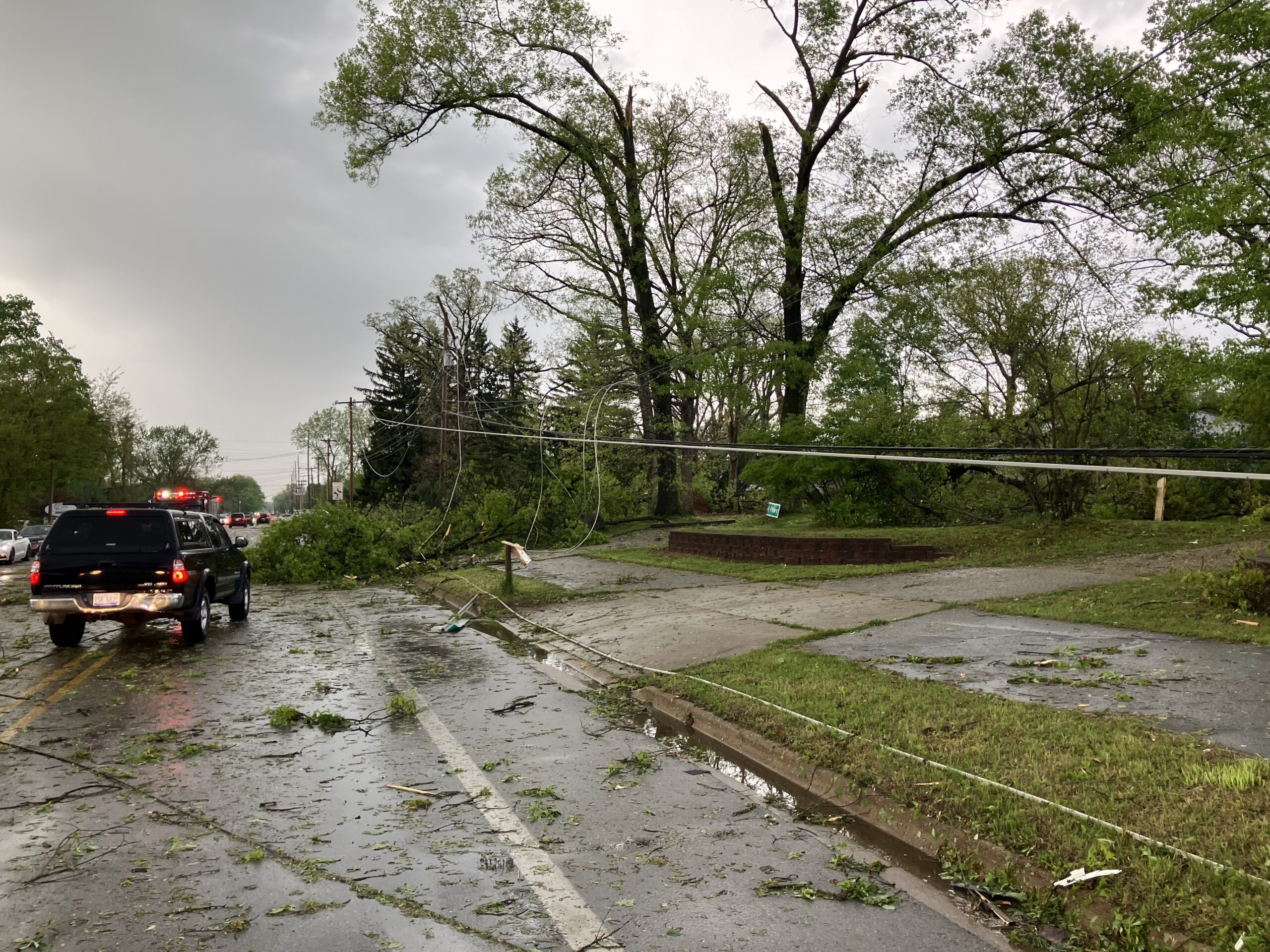 Image of a road littered with leaves and debris, with emergency response vehicle parked in the center of the road.