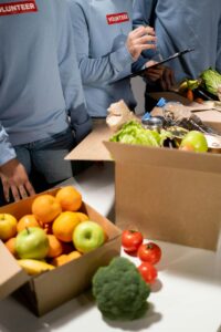 Three people standing at a table with boxes of food and prepare fruits, vegetables, water and other foods to hand out to people in need.