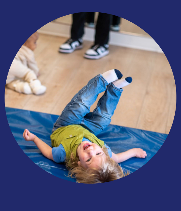 Child rolls on a blue mat, while a baby crawls in the background.