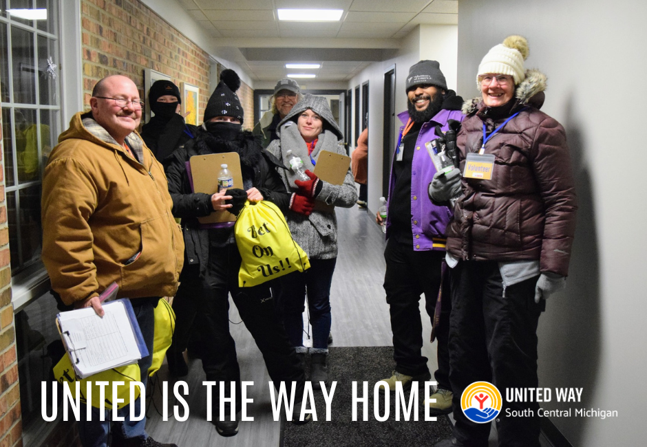 A group of seven people in winter gear pose for a group photo in a hallway.