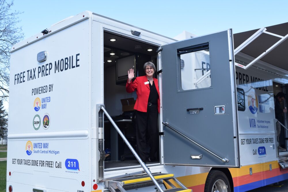 Woman leans out the door of a mobile tax clinic bus, waving.