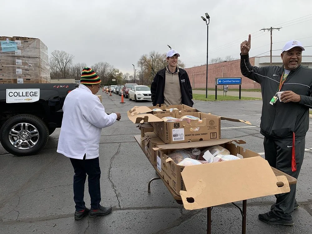 Three people pack boxes outdoors on a table.