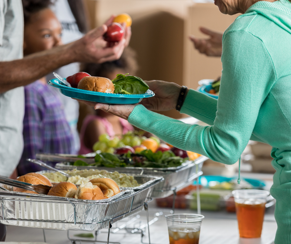 A table of food with people on both sides holding plates.