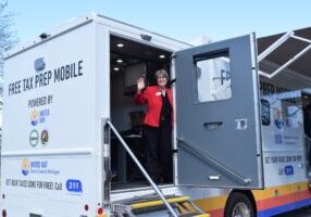 Woman leans out the door of a mobile tax clinic bus, waving.